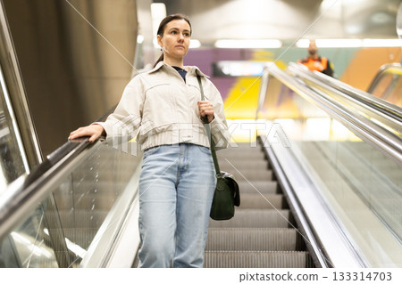 Woman metro passenger on escalator, enters underground public transport station 133314703