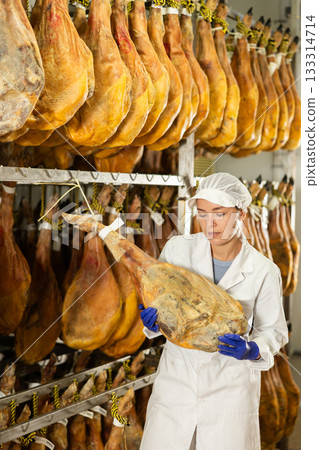 female worker checks the quality of jamon in a factory 133314714
