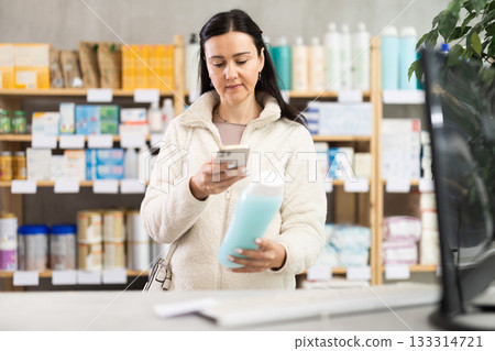 Middle-aged woman scanning QR-code on shampoo in drugstore Middle-aged woman scanning QR-code on shampoo in drugstore 133314721