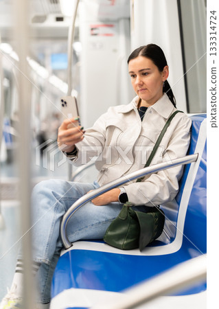 European woman sitting on seat in subway train and using smartphone 133314724