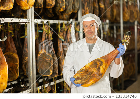 Satisfied male worker at jamon factory shows off finished jamon 133314746