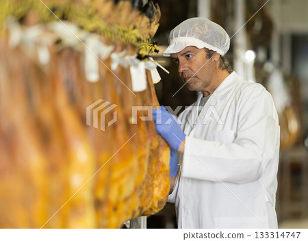 man checks the quality of ham in a factory 133314747