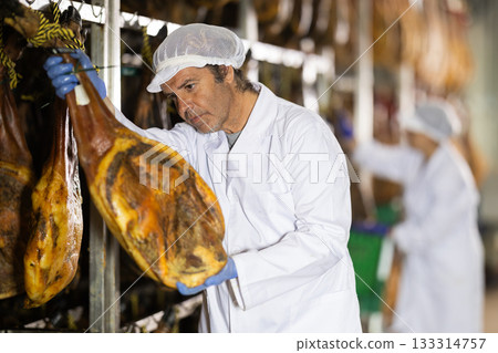 man checks the quality of ham in a factory 133314757