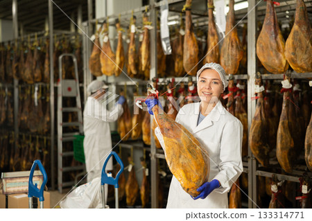 In jamon production shop, girl employee demonstrates final product 133314771