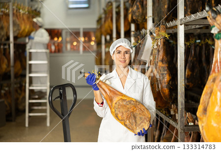 In jamon production shop, woman employee demonstrates final product 133314783