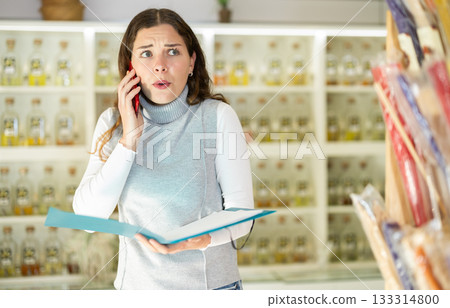 Anxious woman with folder talking on phone in perfume shop 133314800