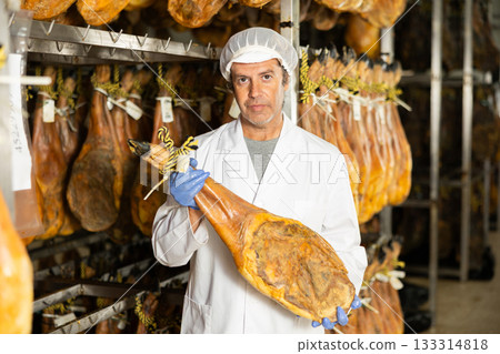 In jamon production shop, man employee demonstrates final product 133314818