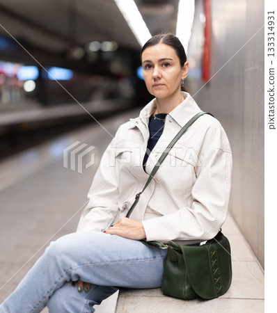 Girl is sitting on metro platform station, waiting for transport to arrive Girl is sitting on metro platform station, waiting for transport to arrive 133314931