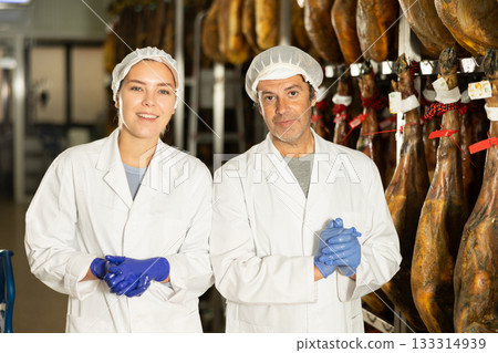Girl and man employee in white uniform, bathrobe and hat, stands in workshop for production of hamon 133314939