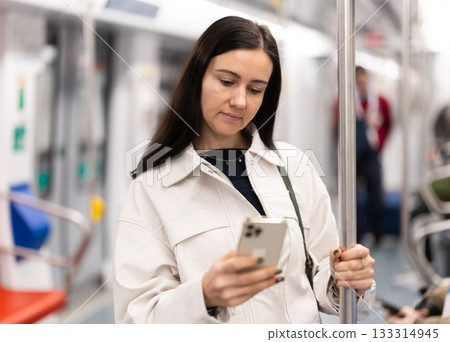 Woman stand in metro carriage, scrolls through social media feed 133314945