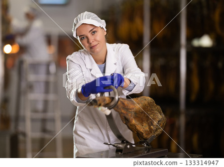 Woman places jamon on jamonero to cut it into appetizing pieces. Ham factory Woman places jamon on jamonero to cut it into appetizing pieces. Ham factory 133314947