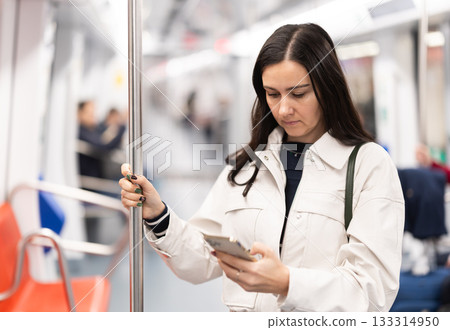 Woman passenger travels in the subway car and uses mobile phone to communicate on social networks 133314950
