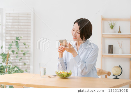 A woman taking a photo of a salad with her smartphone A woman taking a photo of a salad with her smartphone 133315058