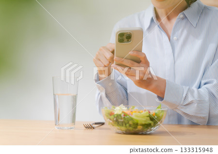 A woman taking a photo of a salad with her smartphone A woman taking a photo of a salad with her smartphone 133315948