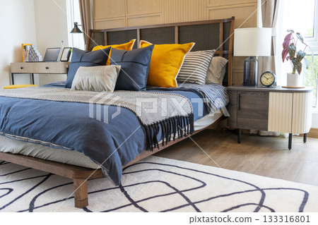 Interior of yellow and blue pillow on cozy modern bedroom with carpet and side table lamp. 133316801