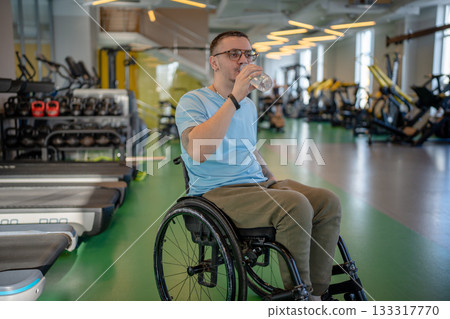 Disabled sportsman in wheelchair resting during powerful workout in gym, drinking water from bottle. Disabled sportsman in wheelchair resting during powerful workout in gym, drinking water from bottle. 133317770