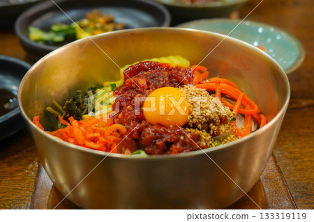 Colorful Ingredients of Jeonju Bibimbap with Raw Beef and Egg Yolk in a Traditional Korean Brass Bowl 133319119