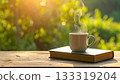 A steaming mug and a book on a natural wooden table 133319204