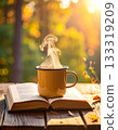 A steaming mug and a book on a natural wooden table 133319209
