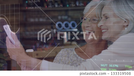 Smiling senior women holding smartphone, taking selfie in living room, with stock charts 133319508