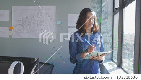 Reviewing Asian designer jotting on tablet with stylus in office by window, blueprints, copy space 133319536