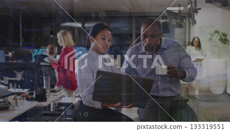 Collaborating woman in striped blouse holding laptop and man holding coffee mug in modern office 133319551