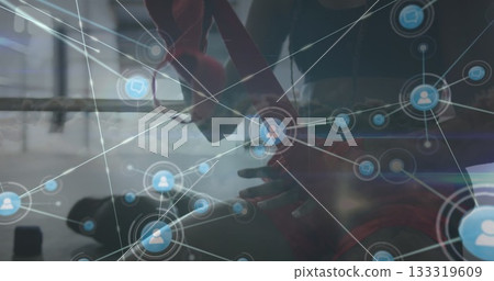 Wrapping boxer in black top adjusting red hand wraps in boxing ring, with digital network overlay 133319609