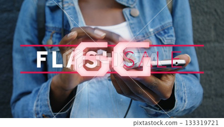 Holding smartphone woman wearing denim jacket against urban grey wall, with neon Flash Sale graphic 133319721