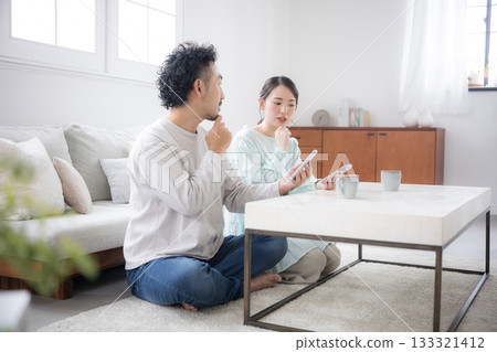 A wife anxiously listens to her husband's conversation while holding her smartphone. A scene of marital communication and financial consultation. 133321412