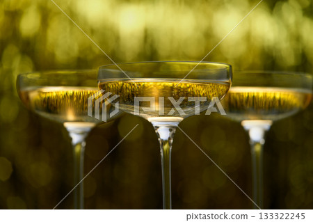 glasses of champagne on golden stylish background with golden bokeh circles with place for text. glasses of champagne on golden stylish background with golden bokeh circles with place for text. 133322245