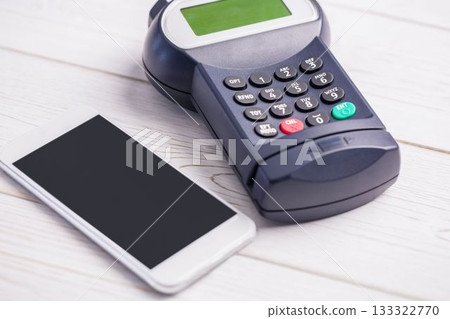 POS terminal with keypad and display is sitting beside smartphone on wooden tabletop, flat design 133322770