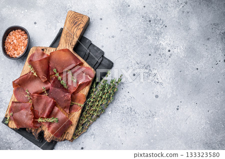 Dried beef meat Cecina, slices of beef jerky on wooden board with herbs. grey background. top view 133323580