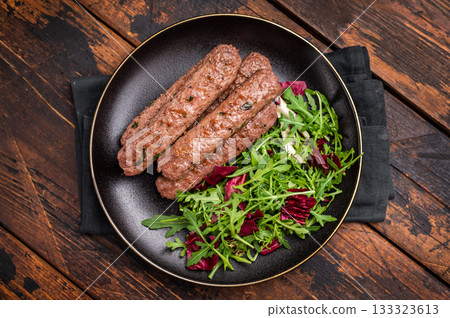 Roasted beef and lamb meat kebabs sausages on plate with salad. wooden background. top view Roasted beef and lamb meat kebabs sausages on plate with salad. wooden background. top view 133323613