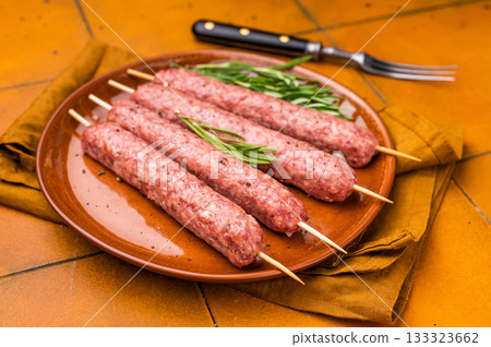 Raw Turkish Urfa kebab skewers on a plate with herbs. orange background. top view Raw Turkish Urfa kebab skewers on a plate with herbs. orange background. top view 133323662