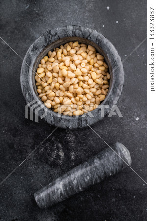 Raw pine nuts placed in a grey stone mortar on a deep textured black backdrop creating a bold rustic look perfect for culinary stock content Raw pine nuts placed in a grey stone mortar on a deep textured black backdrop creating a bold rustic look perfect for culinary stock content 133323837
