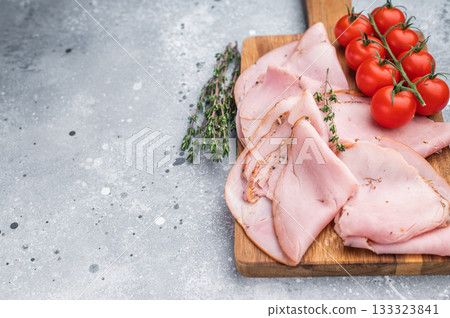 Gourmet deli meat cured pork slices arranged with tomatoes and herbs on rustic wood over a gray background suitable for menus packaging or ads. 133323841