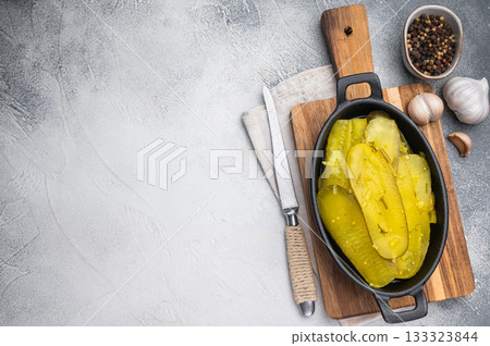 Rustic pickled cucumber slices in cast iron dish with garlic and spices on textured light background, vibrant brined yellow food. 133323844