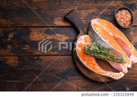 Fresh salmon steaks with thyme on a rustic wooden board creating a warm culinary scene perfect for recipe designs cooking ads and food visuals. Fresh salmon steaks with thyme on a rustic wooden board creating a warm culinary scene perfect for recipe designs cooking ads and food visuals. 133323849