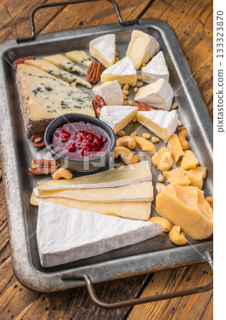 Gourmet cheese platter with assorted textures and nuts arranged on vintage metalware over a wooden background. 133323870