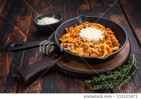 Classic pasta bolognese with savory meat ragu and parmesan shreds served in rustic skillet on vintage wooden surface with herbs. Classic pasta bolognese with savory meat ragu and parmesan shreds served in rustic skillet on vintage wooden surface with herbs. 133323871
