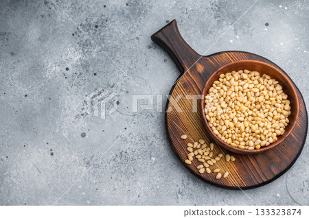 Close view of raw pine nuts in a rustic wooden bowl on a bright white backdrop giving a clean organic feel suitable for culinary and healthy food themes 133323874