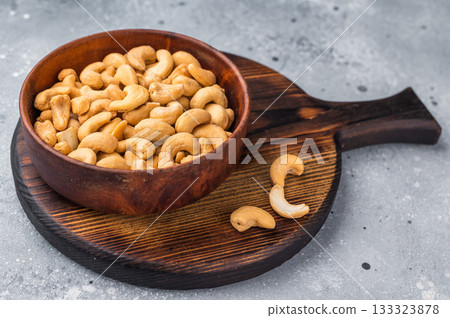 Cashew nuts in a wooden bowl placed on a rustic board against a textured grey background creating a warm natural food scene for culinary stock 133323878