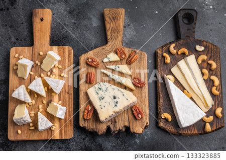 Brie Camembert and Roquefort served on rustic wooden boards with mixed nuts placed over a dark artistic background. 133323885