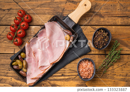 Italian pork charcuterie, slice of ham deli meat and assorted olives arranged on a plate placed against aged wooden boards ideal for commercial culinary layouts. Italian pork charcuterie, slice of ham deli meat and assorted olives arranged on a plate placed against aged wooden boards ideal for commercial culinary layouts. 133323887