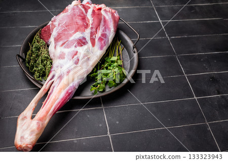 Uncooked whole lamb leg, raw mutton meat with herbs for cooking. black background. top view Uncooked whole lamb leg, raw mutton meat with herbs for cooking. black background. top view 133323943