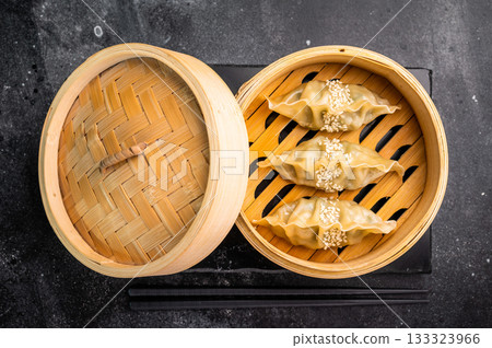Steamed Korean Dumplings with pork meat and vegetables in bamboo steamer. black background. top view Steamed Korean Dumplings with pork meat and vegetables in bamboo steamer. black background. top view 133323966