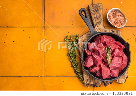 Ready for cooking Diced Elk meat, raw Game Meat in a pan. orange background. top view 133323981