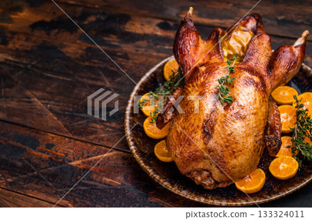 Roast goose with apples and oranges on plate with herbs. wooden background. top view 133324011