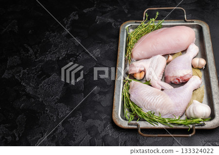Raw chicken assortment: breast, leg, drumstick, and wing with fresh herbs and garlic on a metal tray, on a dark textured background. Copy space. Raw chicken assortment: breast, leg, drumstick, and wing with fresh herbs and garlic on a metal tray, on a dark textured background. Copy space. 133324022