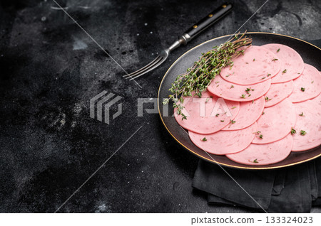 Round slices of pink deli meat (salami/ham) seasoned with thyme, presented on a dark plate for a charcuterie snack or sandwich ingredient. Round slices of pink deli meat (salami/ham) seasoned with thyme, presented on a dark plate for a charcuterie snack or sandwich ingredient. 133324023